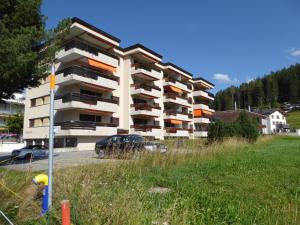 um edifício de apartamentos branco com um parque de estacionamento e um campo em Bündapark em Davos