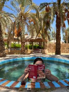 a boy reading a book in a swimming pool at Seliyaa Siwa Inn Hotel in Siwa