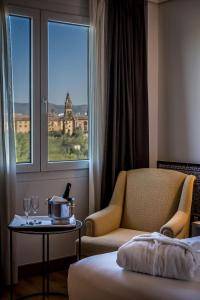 um quarto de hotel com uma cadeira, uma mesa e uma janela em Hesperia Córdoba em Córdoba