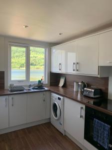 cocina con armarios blancos, fregadero y lavavajillas en Cottage on the Loch, en Arrochar