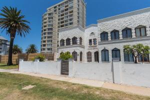 a white building with a palm tree and a tall building at Villas Marina On The Beach in Port Elizabeth