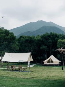 uma tenda e bancos num campo com montanhas ao fundo em NatureLand Campsite em Shenzhen
