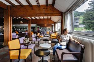 une femme assise sur un canapé dans une pièce avec des chaises et des tables dans l'établissement Belambra Clubs Superbesse - Le Chambourguet, à Super-Besse