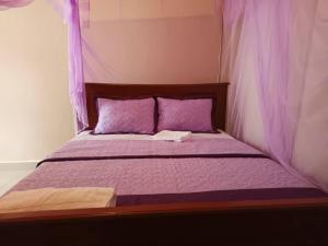 a bed with purple pillows and a book on it at City Cottages Mbale in Mbale