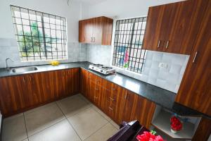 a kitchen with wooden cabinets and a sink and two windows at HISHAMS BHAVAN in Alwaye