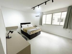 a white bedroom with a bed and a window at Studio Duque Master in Porto Alegre