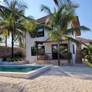 une maison sur la plage avec une piscine et des palmiers dans l'établissement Sand Beach Boutique Villas, à Bwejuu