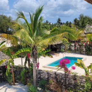 - une vue aérienne sur la piscine du complexe bordée de palmiers et de fleurs dans l'établissement Sand Beach Boutique Villas, à Bwejuu
