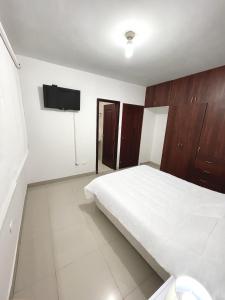 um quarto com uma cama branca e uma televisão de ecrã plano em Casa con Habitación Privada em Guayaquil