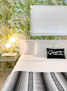 1 dormitorio con cama blanca y papel pintado tropical en Seaspray Surf Lodge, en Vero Beach