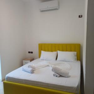 a bed with a yellow headboard and white sheets and pillows at Hotel Eno in Përmet