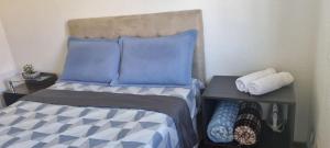 a bed with blue pillows and a side table with towels at Casa Familiar Moradas Pelotas in Pelotas