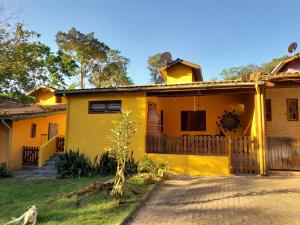 una casa amarilla con un perro parado frente a ella en Mandala casa 3 dorms cond fech piscina churrasqueira en Boicucanga
