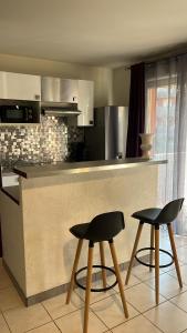 une cuisine avec deux tabourets noirs devant un comptoir dans l'établissement Superbe T2 à Balaruc les Bains, à Balaruc-les-Bains