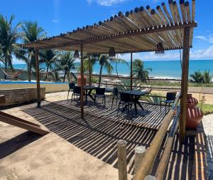 - une table et des chaises sous une pergola sur la plage dans l'établissement Pousada Enseada do Sol, à Jacumã