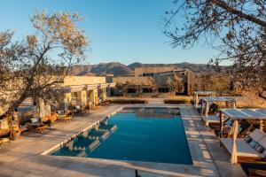 a swimming pool with tables and chairs and mountains in the background at Hotel Andana Winery & Spa in Valle de Guadalupe
