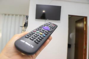 eine Hand mit einer Fernbedienung vor einem TV in der Unterkunft Águas da Barra in Maragogi