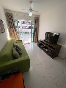 ein Wohnzimmer mit einem grünen Sofa und einem Flachbild-TV in der Unterkunft Apt 3 Minutos Praia do Forte - Ar Condicionado in Cabo Frio