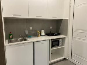 cocina con armarios blancos, fregadero y microondas en Leo's Apartments en Koropíon