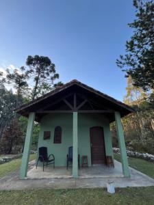 a small green house with two chairs and a door at Pousada Chalés da Lua in Munhoz