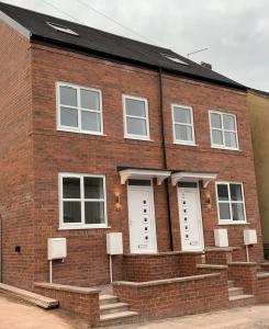 a red brick building with white doors and stairs at 3 Bedroom New House with Wi-Fi Sleep 5 By Home Away From Home in Newcastle under Lyme