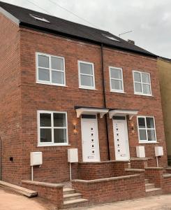 a red brick building with white doors and stairs at 3 Bedroom New House with Wi-Fi Sleep 5 By Home Away From Home - A in Newcastle under Lyme