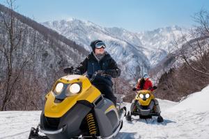 duas pessoas a andar em motos de neve na neve em Holiday Inn Resort Shinano-Omachi Kuroyon, an IHG Hotel em Omachi