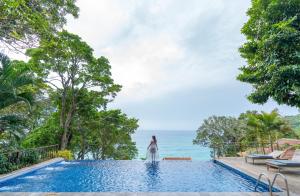Secret Cliff Resort & Restaurant - SHA Plus في شاطئ كارون: امرأة تقف بجوار حمام سباحة يطل على المحيط