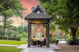 zwei Menschen sitzen an einem Tisch in einem Pavillon in der Unterkunft U Inchantree Kanchanaburi in Kanchanaburi