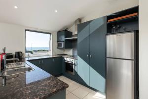 a kitchen with blue cabinets and a stainless steel refrigerator at Longbeach Ocean Paradise in Mount Maunganui