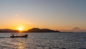 un barco en el agua con la puesta de sol en el fondo en Bleu MATHIS Gili Asahan, en Gili Asahan