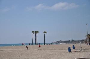 two people walking on a beach with palm trees at Hotel Castilla Alicante in Alicante