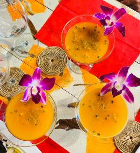 two glasses of orange juice with purple flowers on a table at Guest house Helene in Kata Beach