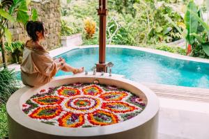 a woman sitting in front of a bathtub covered in flowers at Nau Villa Ubud in Tegalalang