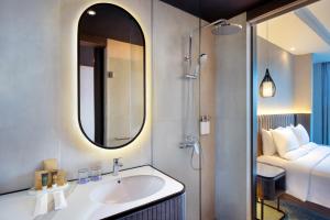 a bathroom with a sink and a mirror and a bed at Novotel Yogyakarta International Airport Kulon Progo in Yogyakarta