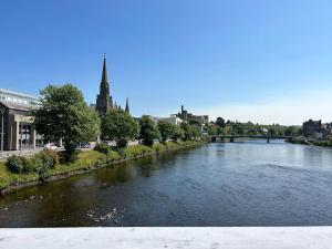 un río en una ciudad con un puente y una iglesia en Jacobite's Retreat, 17th century cottage in the heart of Inverness, en Inverness