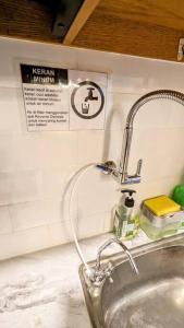 a bathroom sink with a faucet and a sign on the wall at Cottonwood Japandi Apartment at Majesty 509 in Bandung