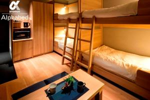 高松市にあるALPHABED INN Takamatsuekimaeの小さな客室で、二段ベッド2台、テーブルが備わります。