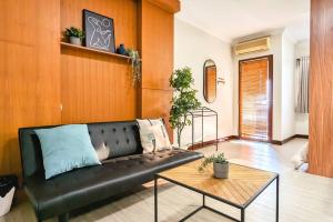 uma sala de estar com um sofá de couro preto e uma mesa em Cottonwood Midcentury Apartment at Majesty 811 em Bandung