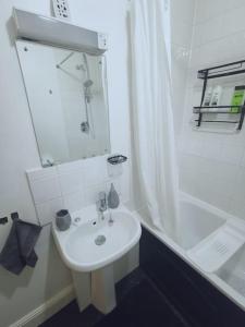 La salle de bains blanche est pourvue d'un lavabo et d'une douche. dans l'établissement Luxe & Stylish Centralised Watford Apt - Fast Wi-Fi & Free Parking Near Harry Potter Studios Tour, à Watford