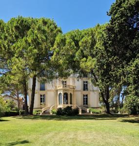 une grande maison avec des arbres devant elle dans l'établissement Château de Bayssan, à Béziers