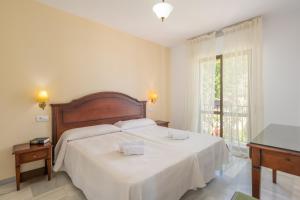 a bedroom with a bed with white sheets and a window at Apartamentos Playamaro in Maro