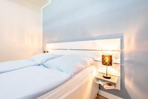 a white bedroom with a bed and a lamp at Steger-Hüs Wohnung 02 in Rantum