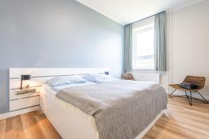 a white bedroom with a bed and a chair at Steger-Hüs Wohnung 19 in Rantum