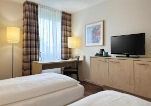 a hotel room with a bed and a desk with a television at Mercure Hotel Düsseldorf Süd in Düsseldorf