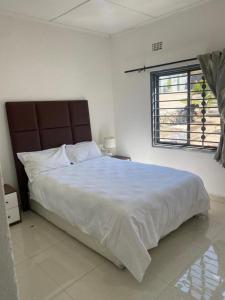 a white bedroom with a large bed and a window at Swiss Luxury Apartments in Ndola