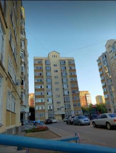 un gran edificio de apartamentos con coches aparcados en un aparcamiento en Zhenis street, en Astana