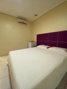 een slaapkamer met een wit bed met een paars hoofdeinde bij Pousada Paraíso in Teresina