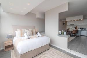 a white bedroom with a large bed and a kitchen at Seaside Studio in Mouille Point in Cape Town