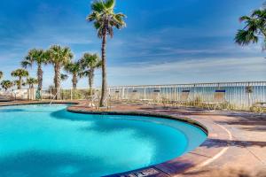 a swimming pool with palm trees in front of a fence at Splash Beach Resort by Panhandle Getaways in Panama City Beach